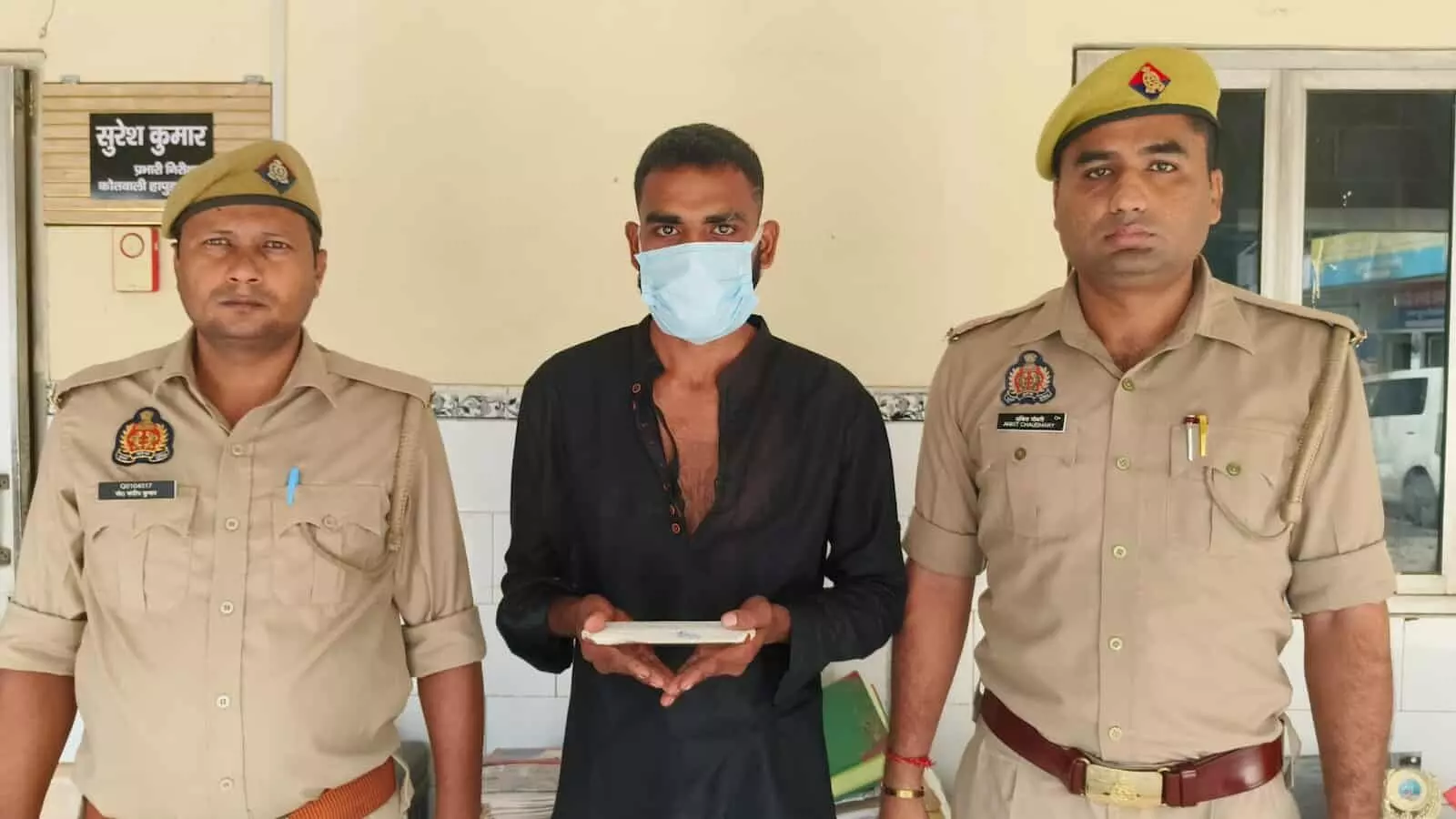 तस्वीर में बाएं और दाएं पुलिसकर्मी खड़े हैं, जबकि बीच में मास्क पहने आरोपी व्यक्ति उनके साथ खड़ा है। तस्वीर में बाएं और दाएं पुलिसकर्मी खड़े हैं, जबकि बीच में मास्क पहने आरोपी व्यक्ति उनके साथ खड़ा है।