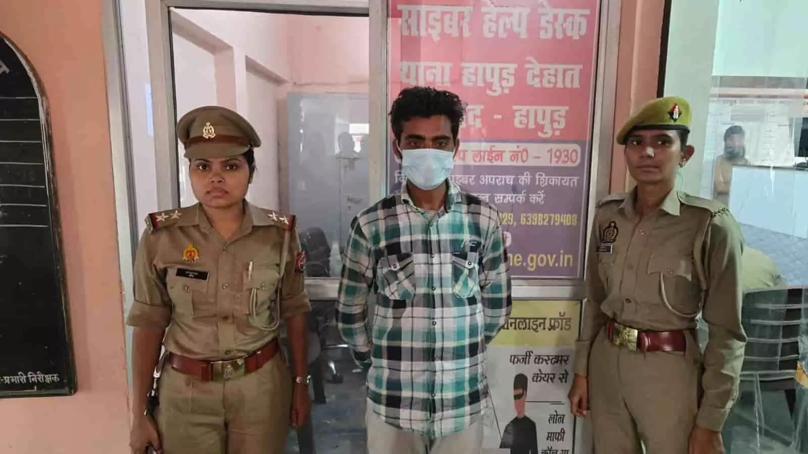 तस्वीर में बाएं और दाएं महिला पुलिस अधिकारी तथा बीच में मास्क लगाए एक युवक थाने में खड़ा है। तस्वीर में बाएं और दाएं महिला पुलिस अधिकारी तथा बीच में मास्क लगाए एक युवक थाने में खड़ा है।
