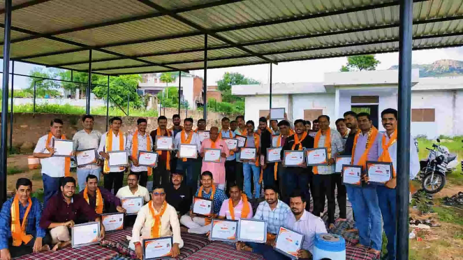तस्वीर में नीचे दरी पर बैठे हुए और पीछे खड़े हुए कई लोग हाथों में प्रमाण पत्र थामे दिखाई दे रहे हैं। तस्वीर में नीचे दरी पर बैठे हुए और पीछे खड़े हुए कई लोग हाथों में प्रमाण पत्र थामे दिखाई दे रहे हैं।