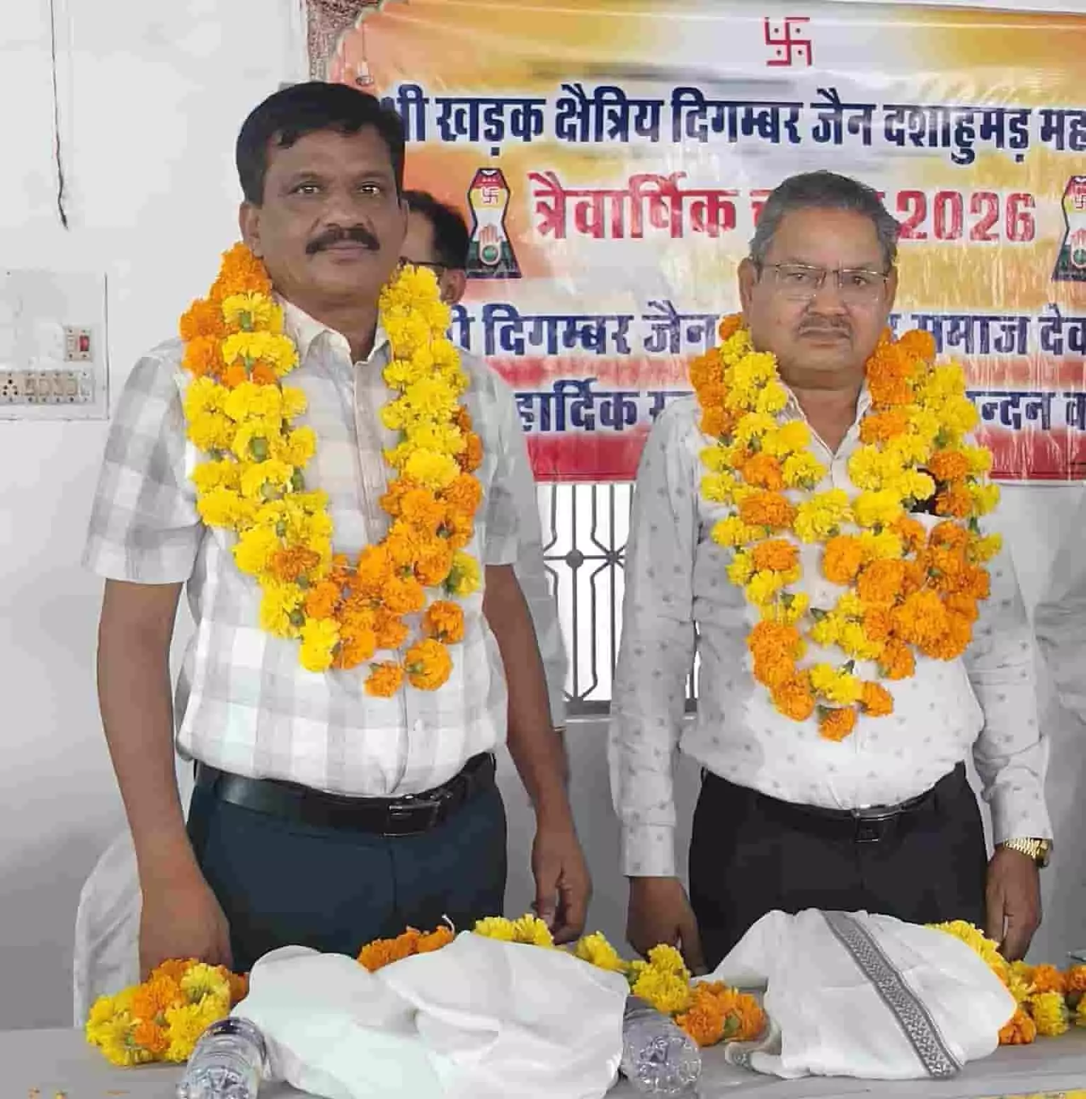 तस्वीर में सफेद शर्ट पहने हुए दो व्यक्ति गले में गेंदे के फूलों की माला डाले हुए खड़े दिखाई दे रहे हैं। तस्वीर में सफेद शर्ट पहने हुए दो व्यक्ति गले में गेंदे के फूलों की माला डाले हुए खड़े दिखाई दे रहे हैं।