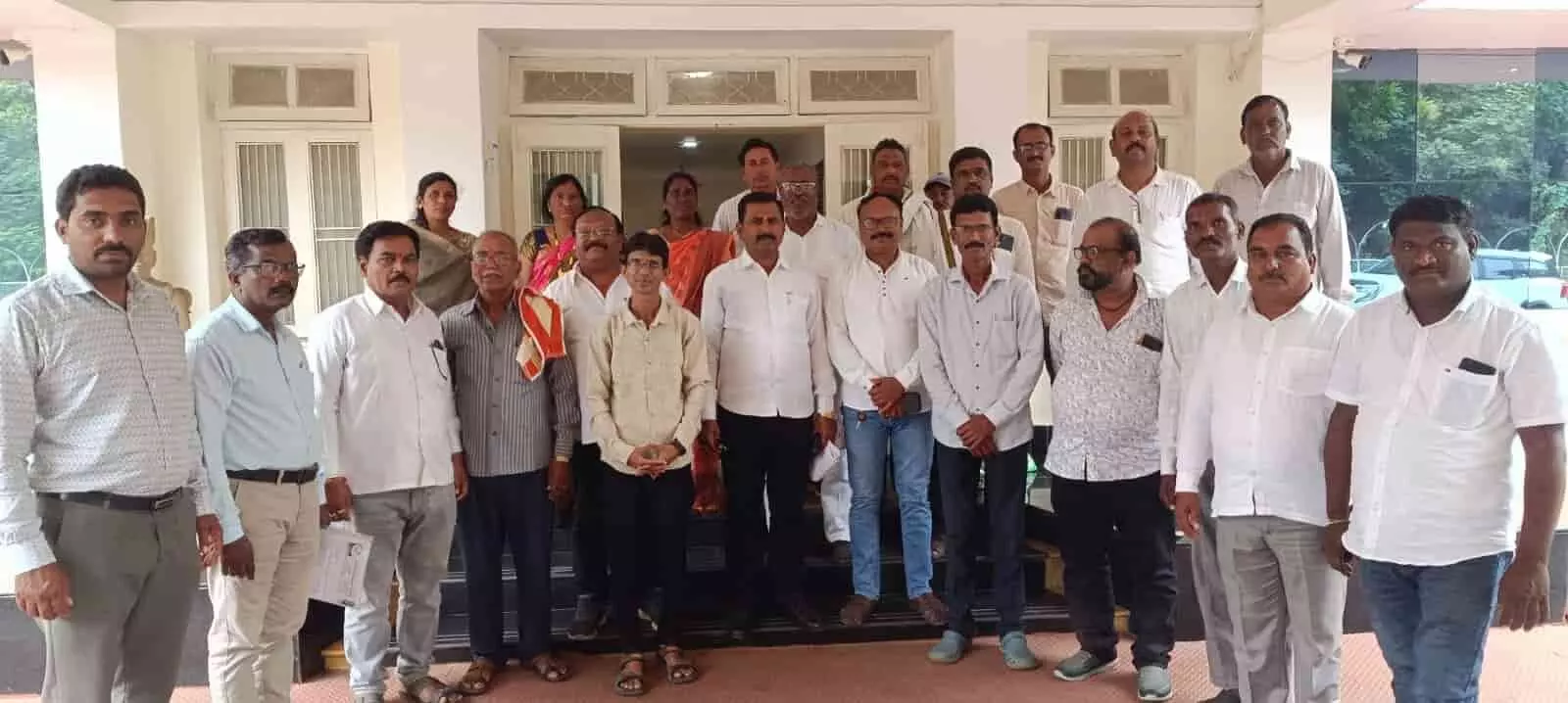 तस्वीर में सफेद और हल्के रंगों की शर्ट तथा पैंट पहने हुए कई पुरुष और महिलाएं एक इमारत के सामने खड़े दिखाई दे रहे हैं। तस्वीर में सफेद और हल्के रंगों की शर्ट तथा पैंट पहने हुए कई पुरुष और महिलाएं एक इमारत के सामने खड़े दिखाई दे रहे हैं।