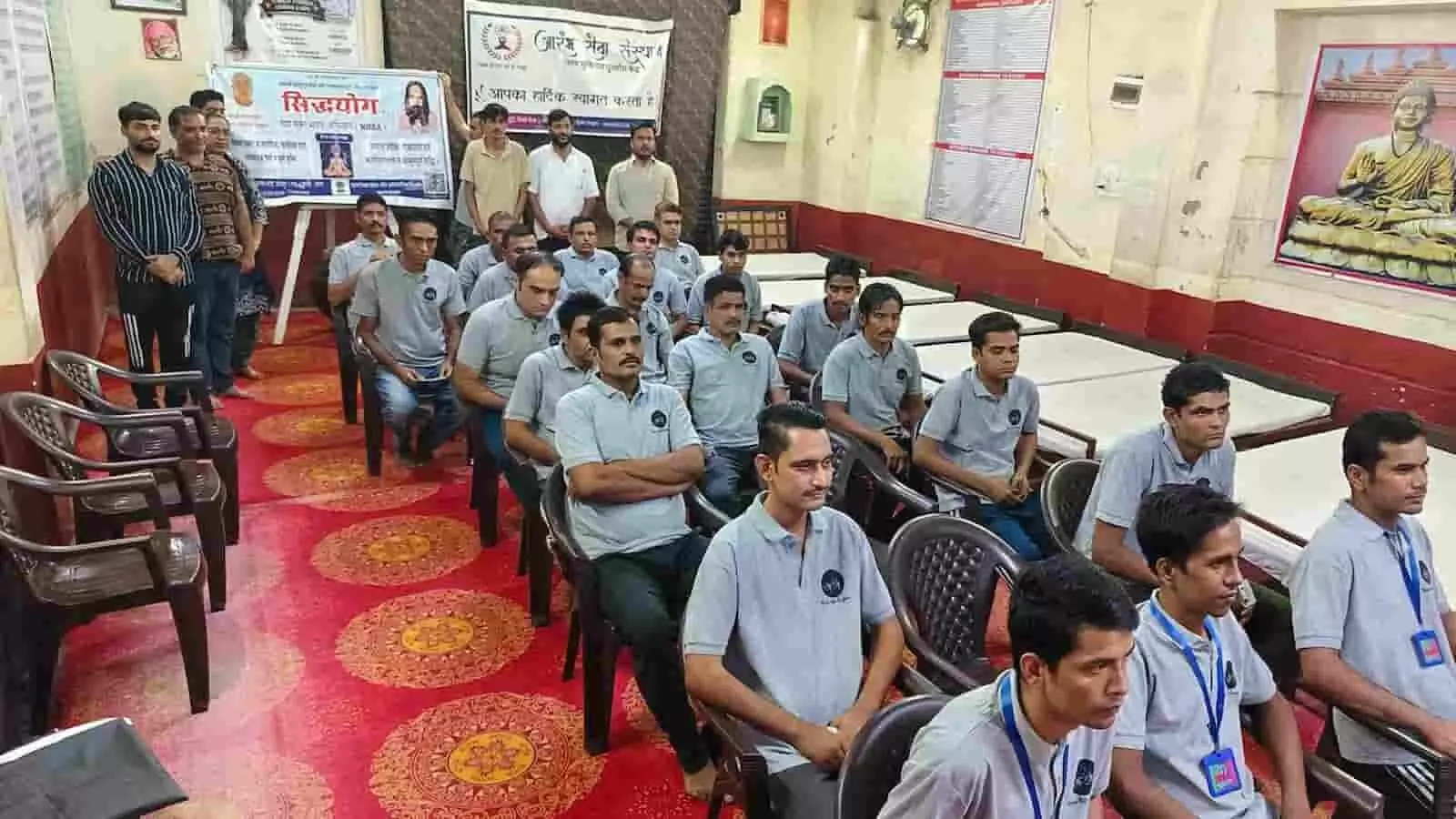 तस्वीर में दिख रही एक सभा में कई पुरुष नीली टी-शर्ट पहनकर कुर्सियों पर बैठे हुए हैं। तस्वीर में दिख रही एक सभा में कई पुरुष नीली टी-शर्ट पहनकर कुर्सियों पर बैठे हुए हैं।