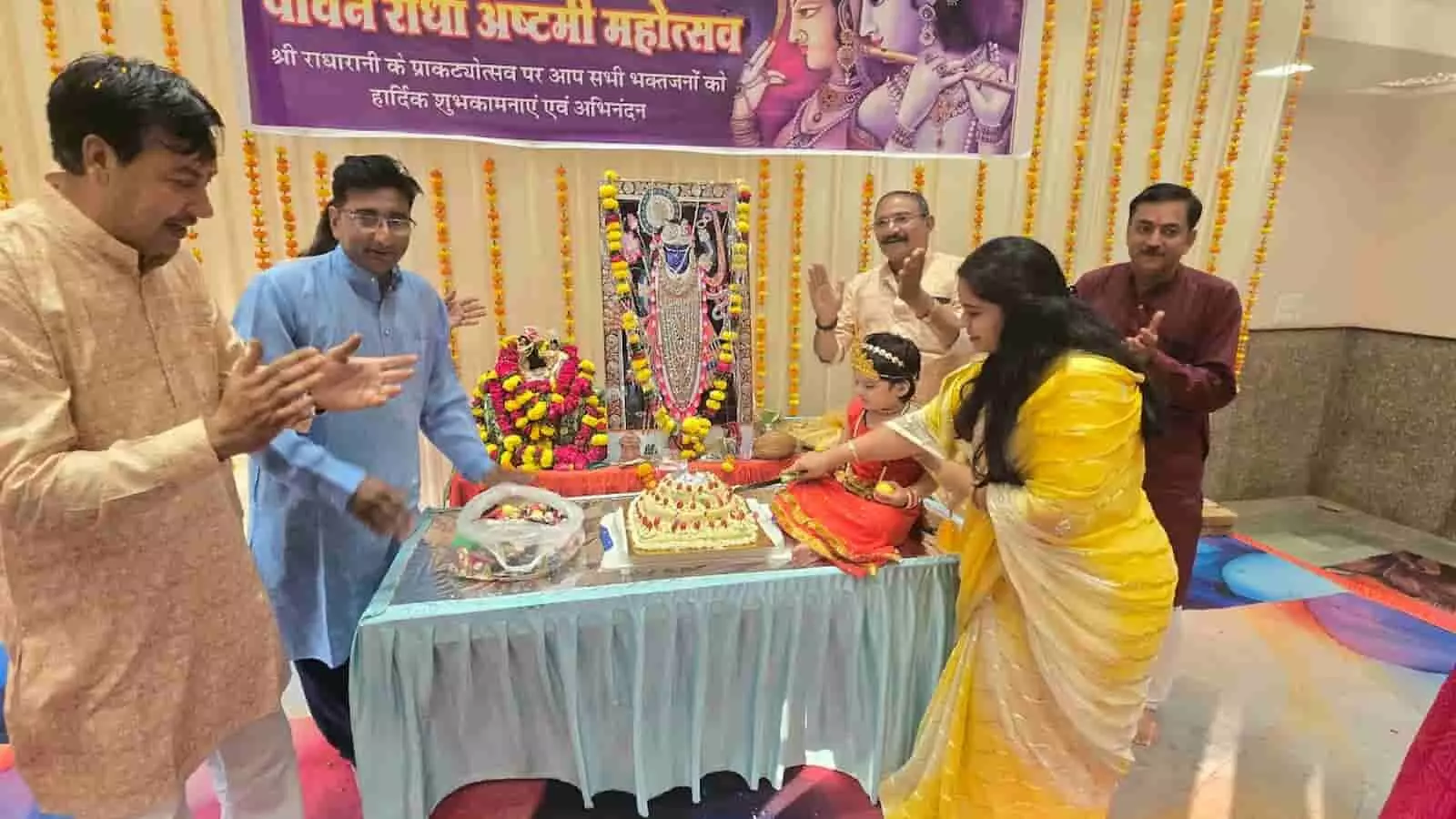 तस्वीर में बाएं से दाएं खड़े पुरुष, बीच में मेज पर सजा केक काटते लोग और पीछे भगवान की तस्वीर नजर आ रही है। तस्वीर में बाएं से दाएं खड़े पुरुष, बीच में मेज पर सजा केक काटते लोग और पीछे भगवान की तस्वीर नजर आ रही है।