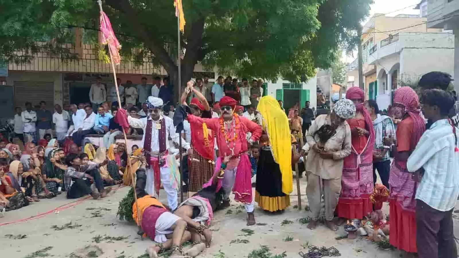 तस्वीर में पारंपरिक वेशभूषा पहने लोक कलाकार खुले मैदान में दर्शकों के सामने गवरी नाटक प्रस्तुत कर रहे हैं। तस्वीर में पारंपरिक वेशभूषा पहने लोक कलाकार खुले मैदान में दर्शकों के सामने गवरी नाटक प्रस्तुत कर रहे हैं।