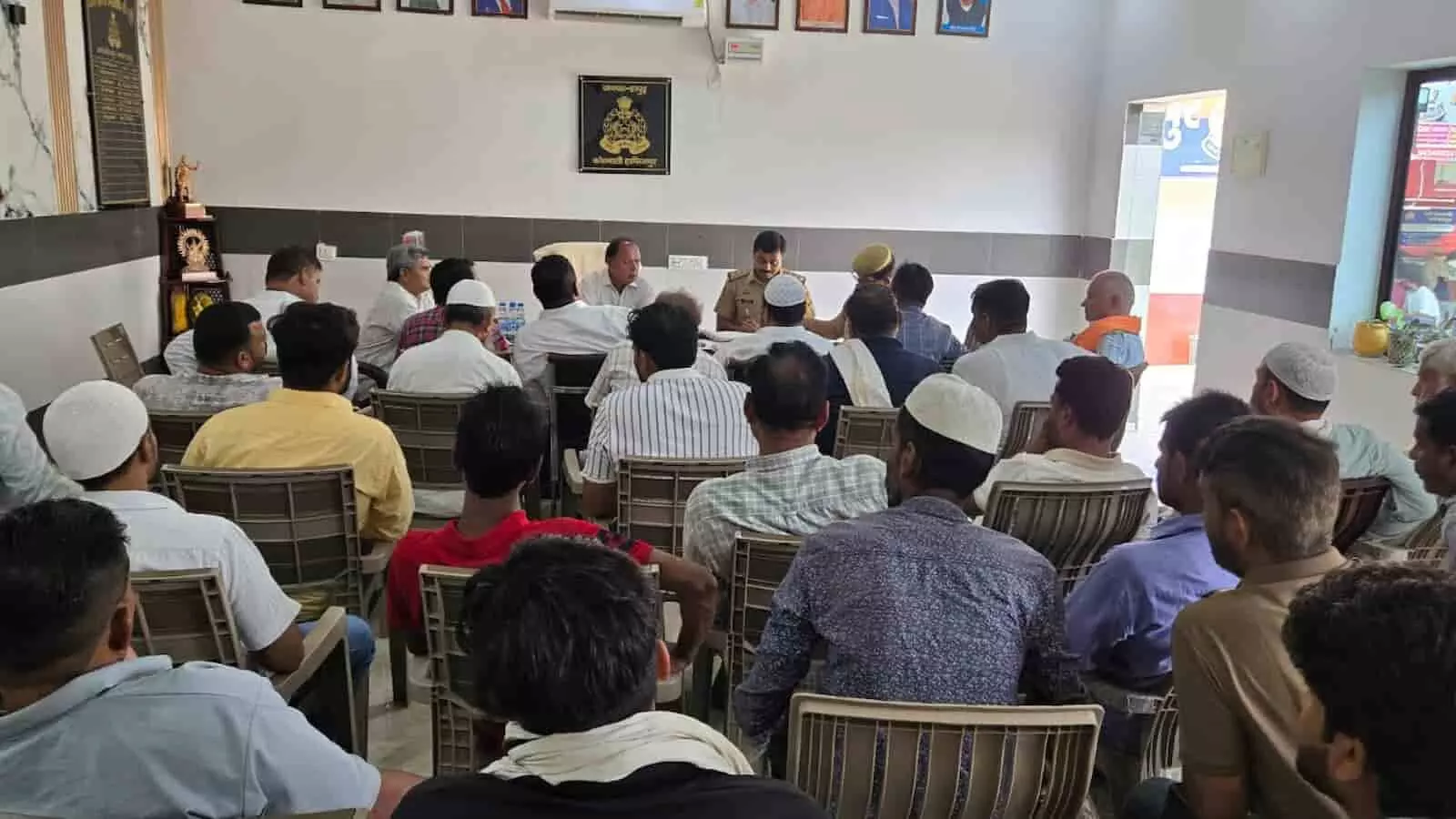 तस्वीर में दिख रही बैठक में पुलिस अधिकारी और स्थानीय नागरिक कमरे में मौजूद हैं। तस्वीर में दिख रही बैठक में पुलिस अधिकारी और स्थानीय नागरिक कमरे में मौजूद हैं।