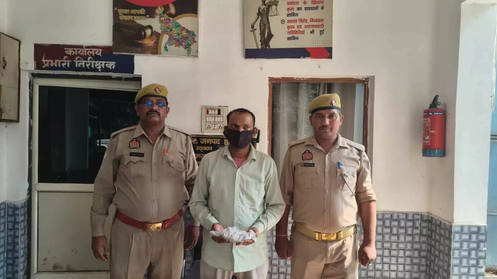 तस्वीर में दो पुलिस अधिकारी एक आरोपी व्यक्ति के साथ पुलिस कार्यालय के बाहर खड़े हैं। तस्वीर में दो पुलिस अधिकारी एक आरोपी व्यक्ति के साथ पुलिस कार्यालय के बाहर खड़े हैं।