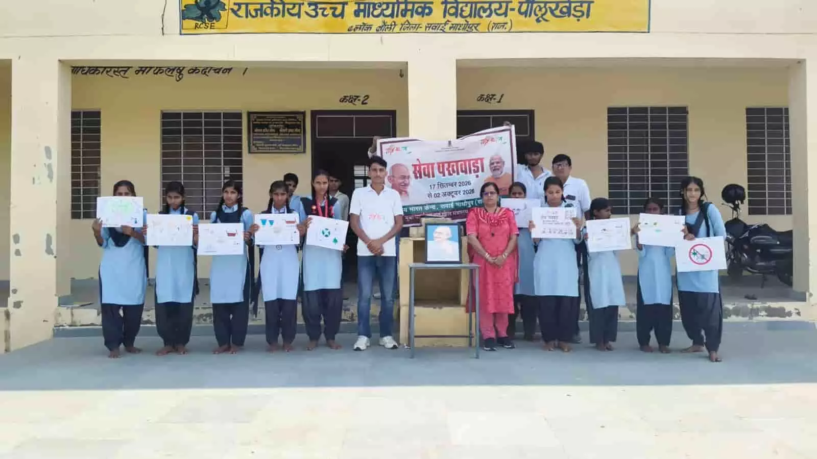 तस्वीर में पीलूखेड़ा स्कूल के विद्यार्थी और शिक्षक बैनर के साथ चित्रकारी शीट्स प्रदर्शित करते हुए खड़े हैं। तस्वीर में पीलूखेड़ा स्कूल के विद्यार्थी और शिक्षक बैनर के साथ चित्रकारी शीट्स प्रदर्शित करते हुए खड़े हैं।