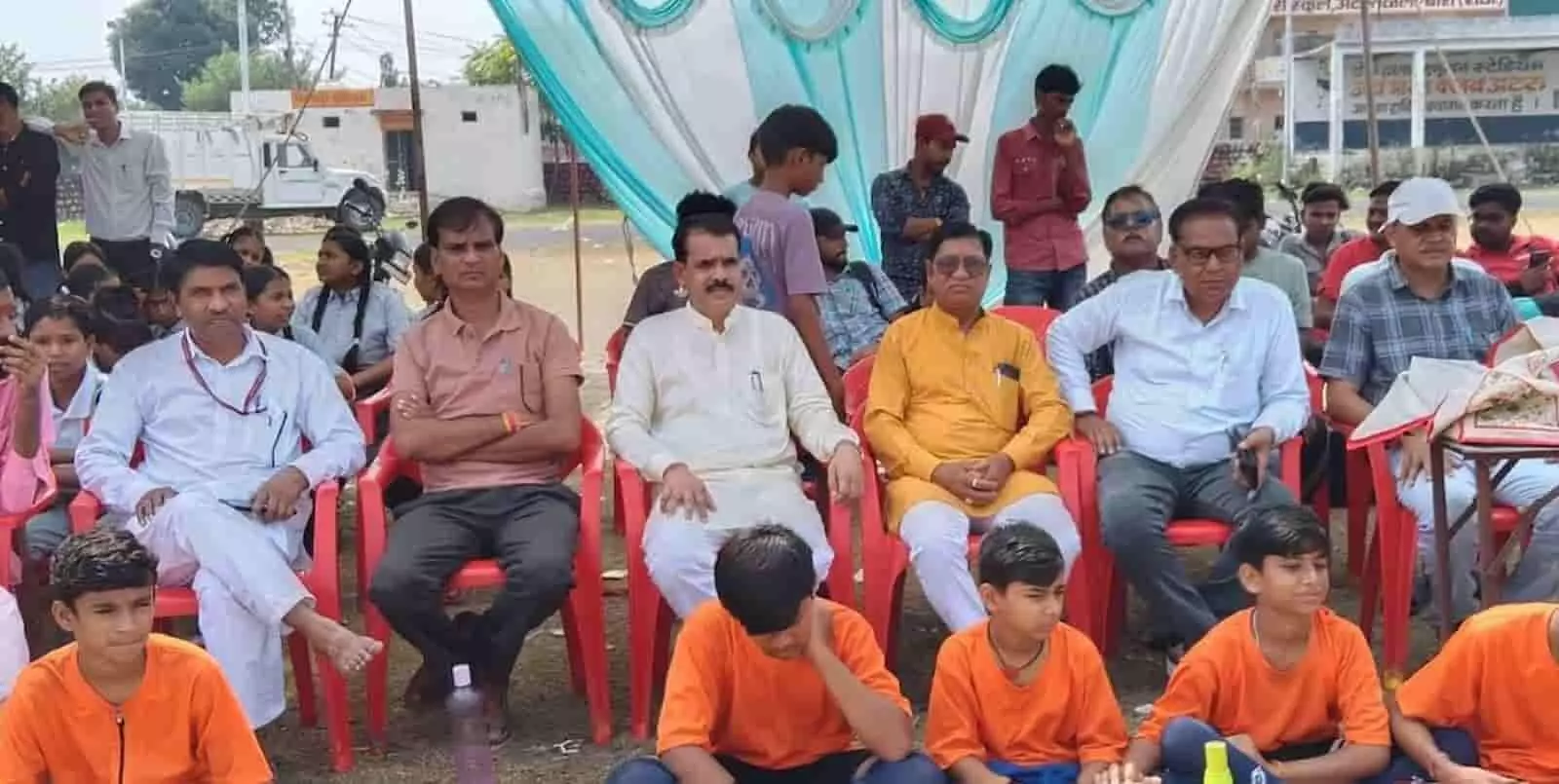 तस्वीर में दिख रही एक आयोजन स्थल की जगह पर अतिथि कुर्सियों पर तथा खिलाड़ी जमीन पर बैठे हैं। तस्वीर में दिख रही एक आयोजन स्थल की जगह पर अतिथि कुर्सियों पर तथा खिलाड़ी जमीन पर बैठे हैं।