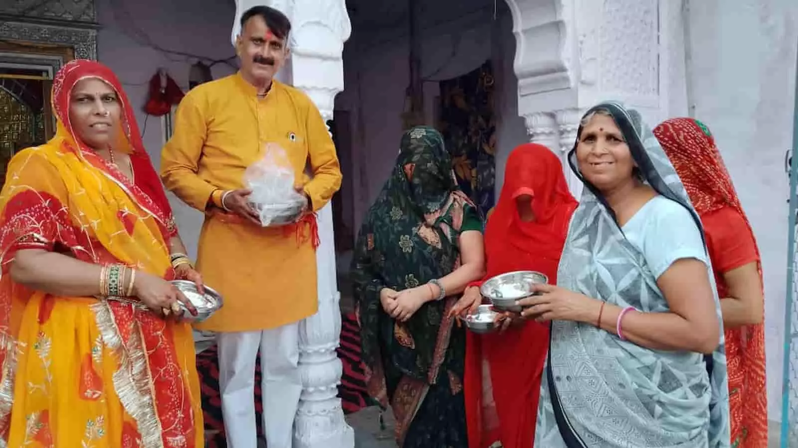 तस्वीर में मंदिर के सामने खड़े पुरुष और महिला श्रद्धालु हाथ में स्टील के बर्तन लिए हुए हैं। तस्वीर में मंदिर के सामने खड़े पुरुष और महिला श्रद्धालु हाथ में स्टील के बर्तन लिए हुए हैं।