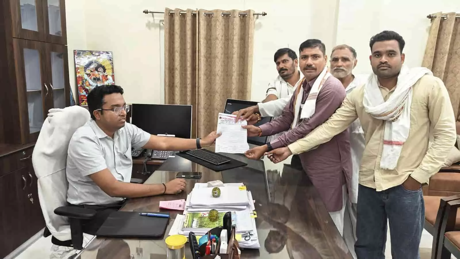 तस्वीर में खड़े हुए लोग एक मेज पर बैठे अधिकारी को लिखित ज्ञापन दे रहे हैं और कार्यालय का कमरा नजर आ रहा है। तस्वीर में खड़े हुए लोग एक मेज पर बैठे अधिकारी को लिखित ज्ञापन दे रहे हैं और कार्यालय का कमरा नजर आ रहा है।