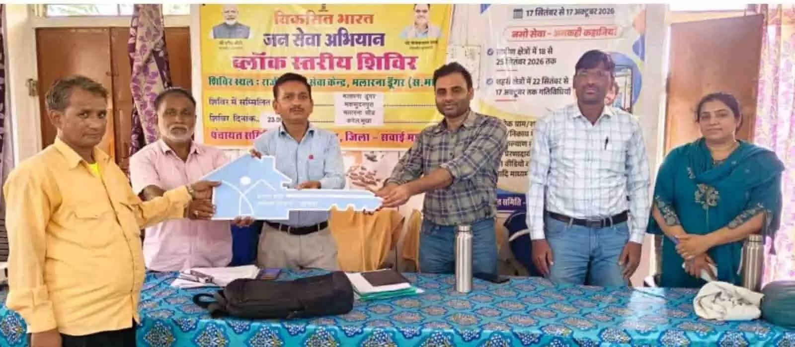 तस्वीर में दिख रही टेबल के पीछे खड़े अधिकारी व्यक्ति को चाबी का कटआउट दे रहे हैं। तस्वीर में दिख रही टेबल के पीछे खड़े अधिकारी व्यक्ति को चाबी का कटआउट दे रहे हैं।