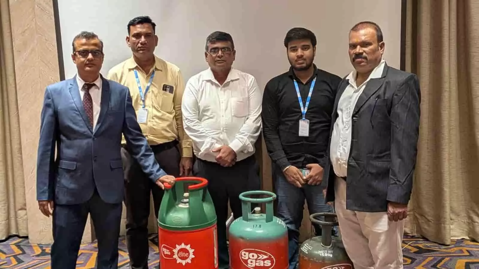 तस्वीर में पाँच व्यक्ति इंडोर सेटिंग में GoGas एलपीजी सिलेंडरों के पास खड़े हैं। तस्वीर में पाँच व्यक्ति इंडोर सेटिंग में GoGas एलपीजी सिलेंडरों के पास खड़े हैं।