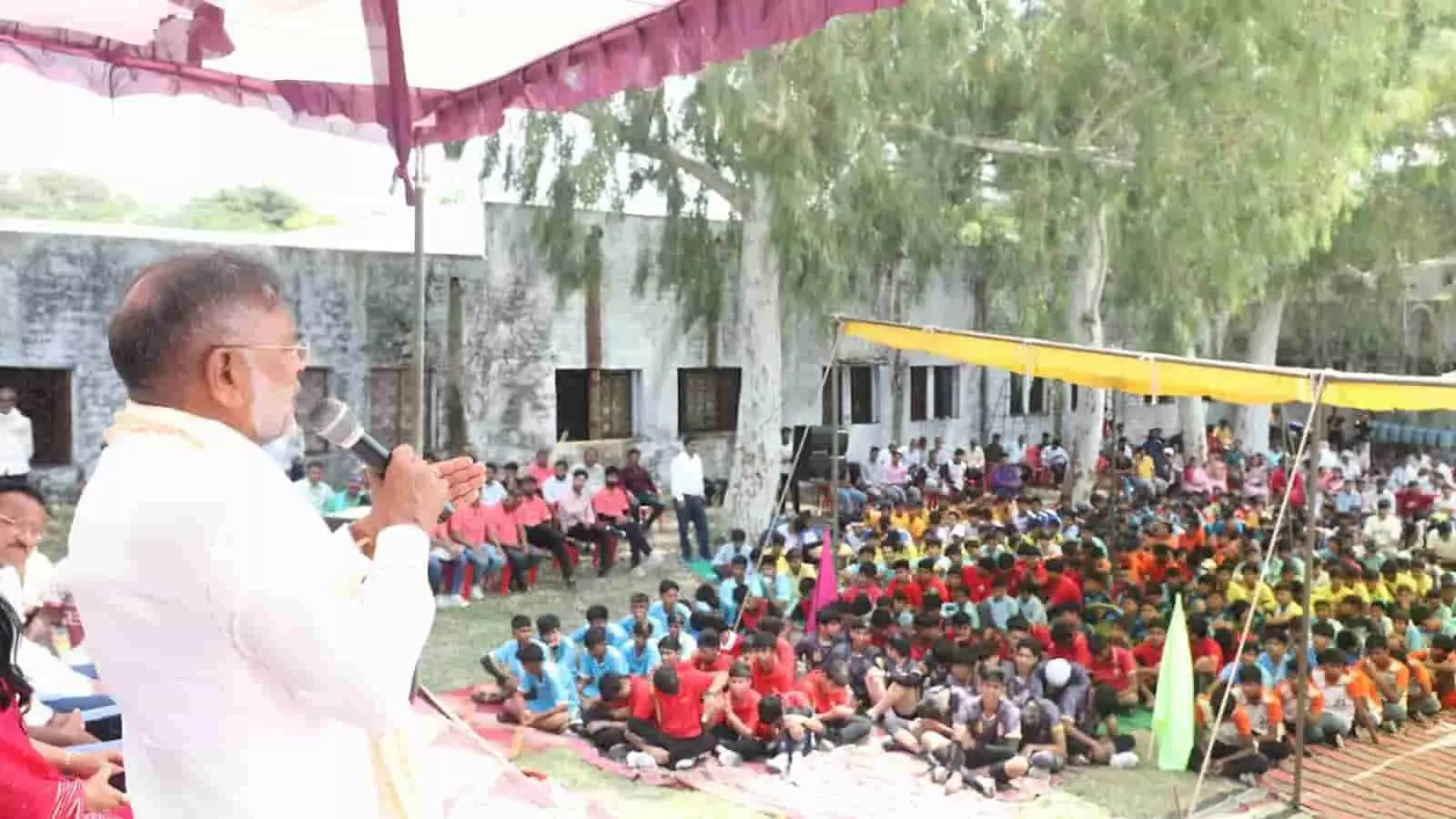 एक खुले मैदान में मंच से सफेद परिधान पहने हीरालाल नागर उपस्थित भीड़ को संबोधित कर रहे हैं। एक खुले मैदान में मंच से सफेद परिधान पहने हीरालाल नागर उपस्थित भीड़ को संबोधित कर रहे हैं।