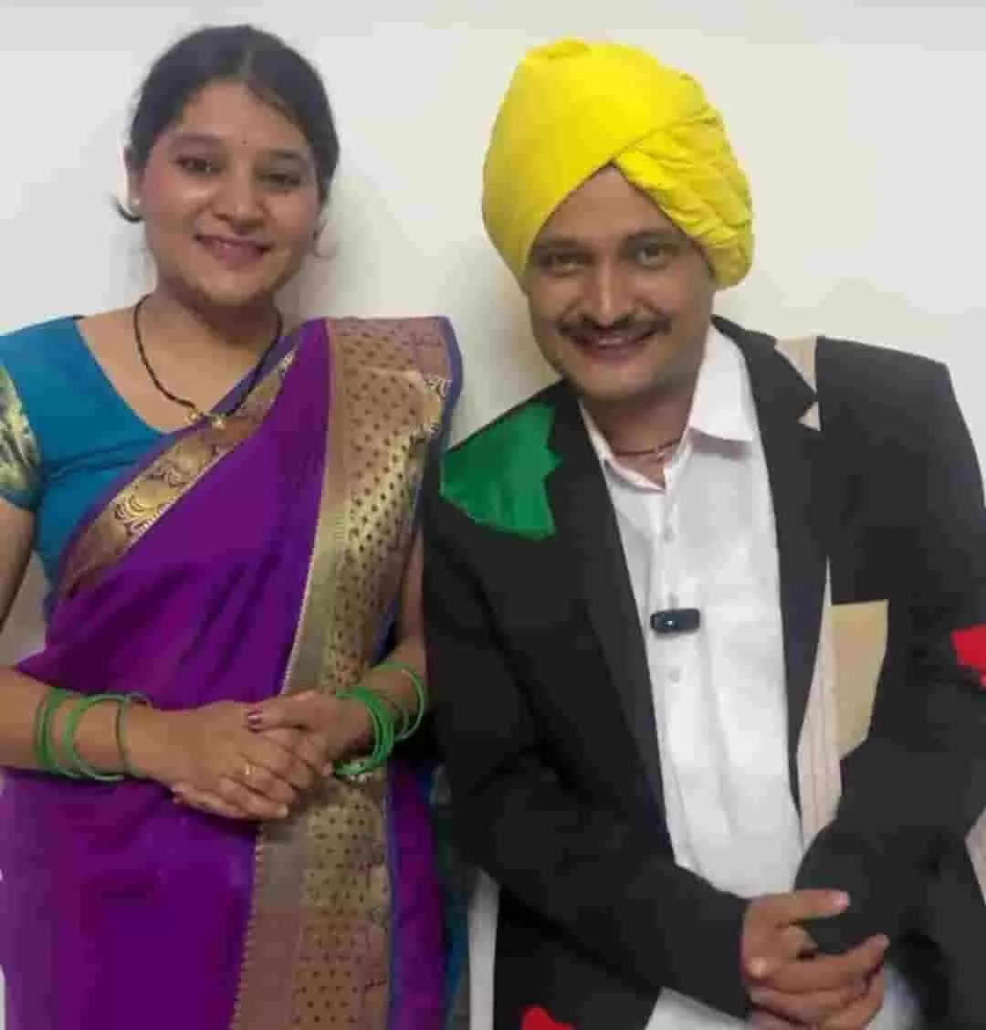 तस्वीर में बाएं तरफ बैंगनी साड़ी पहने महिला और दाएं तरफ पीले रंग की पगड़ी और कोट पहने कलाकार खड़े दिखाई दे रहे हैं। तस्वीर में बाएं तरफ बैंगनी साड़ी पहने महिला और दाएं तरफ पीले रंग की पगड़ी और कोट पहने कलाकार खड़े दिखाई दे रहे हैं।