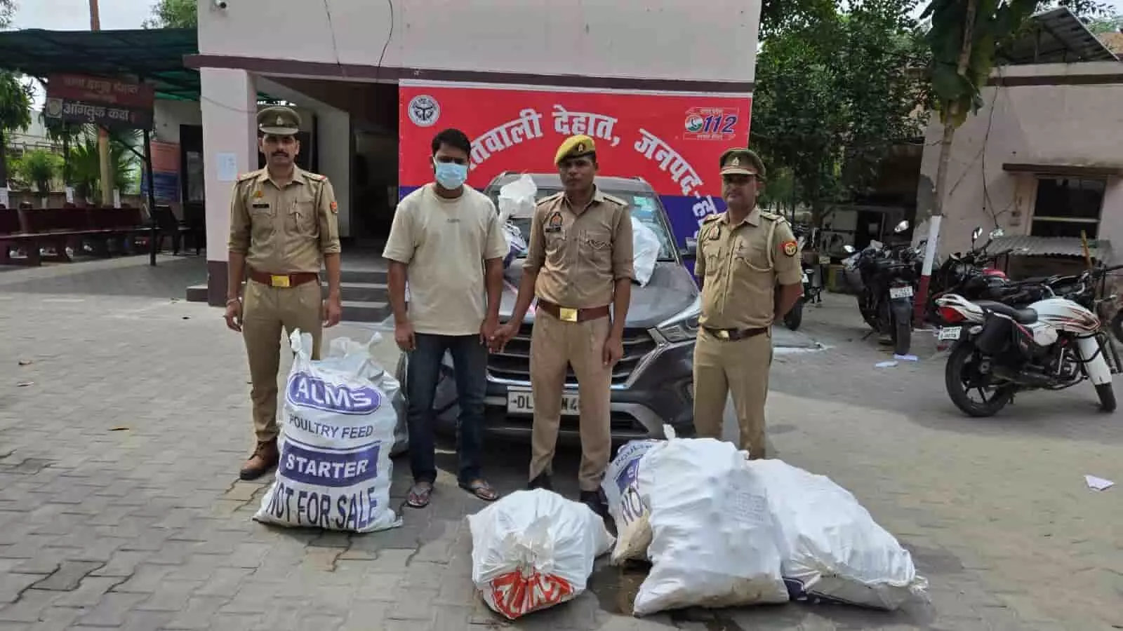 तस्वीर में तीन पुलिसकर्मी, मास्क पहने एक अभियुक्त और पुलिस स्टेशन के सामने रखी बोरियां दिख रही हैं। तस्वीर में तीन पुलिसकर्मी, मास्क पहने एक अभियुक्त और पुलिस स्टेशन के सामने रखी बोरियां दिख रही हैं।