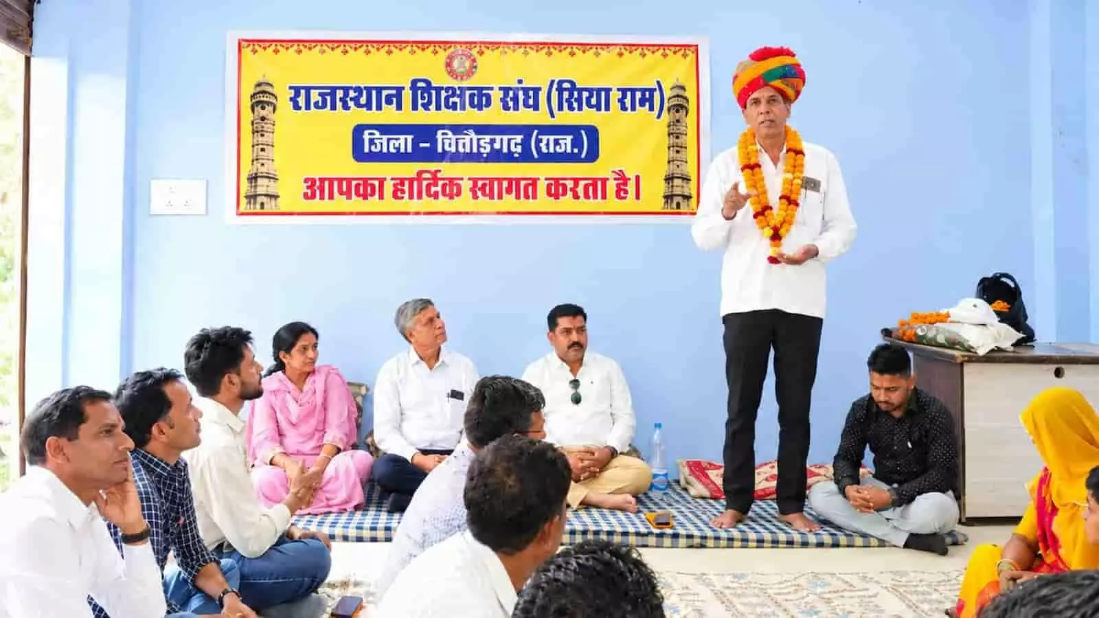 तस्वीर में दिख रही बैठक के दौरान साफा और माला पहने व्यक्ति अन्य सदस्यों को संबोधित कर रहे हैं। तस्वीर में दिख रही बैठक के दौरान साफा और माला पहने व्यक्ति अन्य सदस्यों को संबोधित कर रहे हैं।