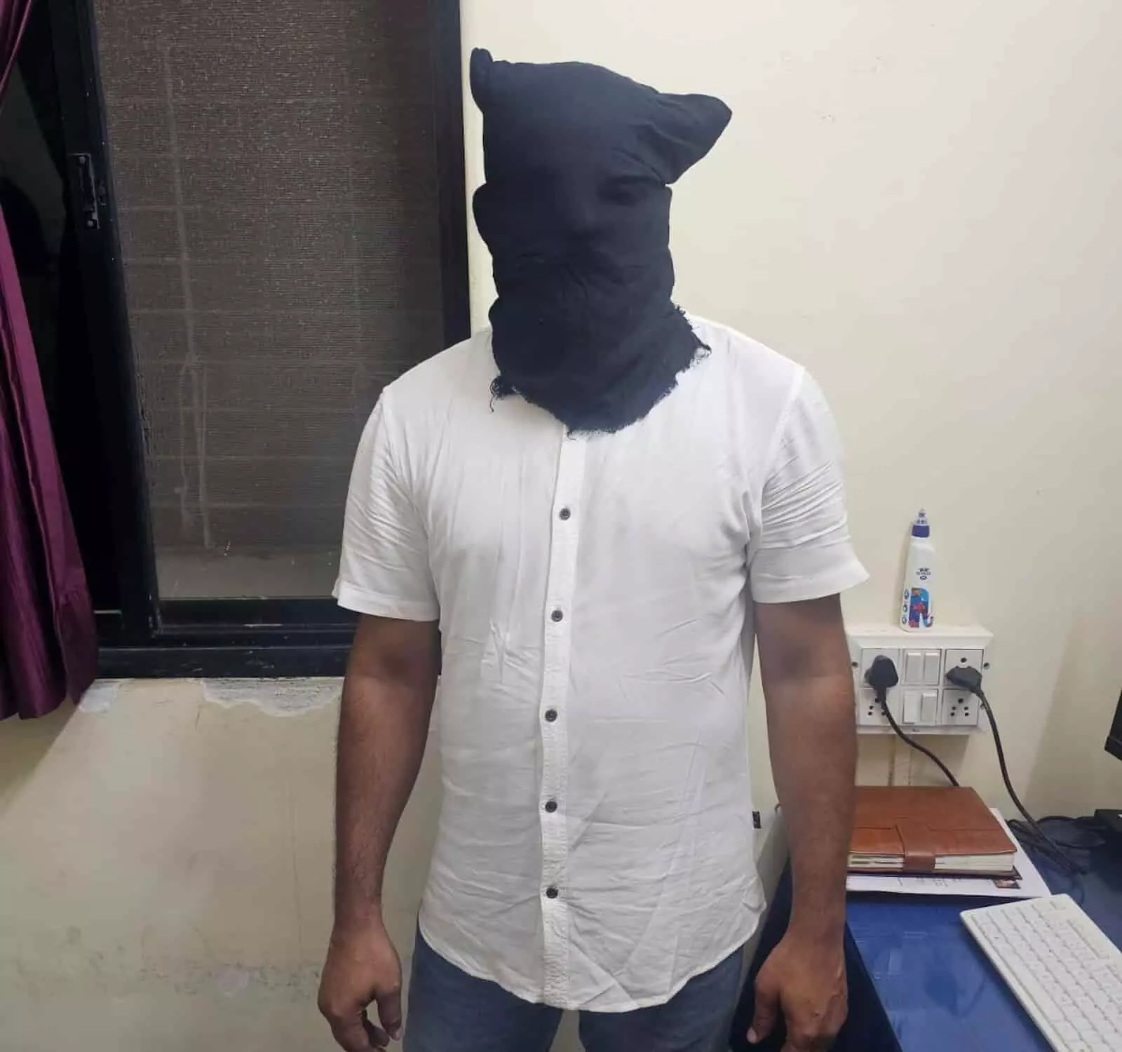 तस्वीर में दिख रही एक व्यक्ति की आकृति पुलिस हिरासत में चेहरे पर काला कपड़ा बांधे खड़ी है। तस्वीर में दिख रही एक व्यक्ति की आकृति पुलिस हिरासत में चेहरे पर काला कपड़ा बांधे खड़ी है।
