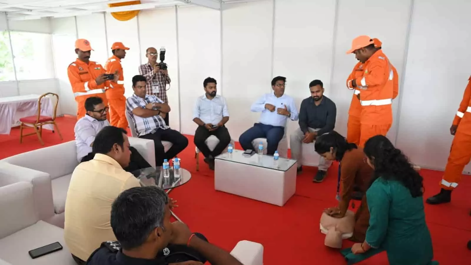 तस्वीर में दिख रही सफेद टी-शर्ट और ओरेंज ड्रेस पहने आपदा प्रबंधन टीम बैठक हॉल में सीपीआर और आपातकालीन तकनीक सीख रही है। तस्वीर में दिख रही सफेद टी-शर्ट और ओरेंज ड्रेस पहने आपदा प्रबंधन टीम बैठक हॉल में सीपीआर और आपातकालीन तकनीक सीख रही है।