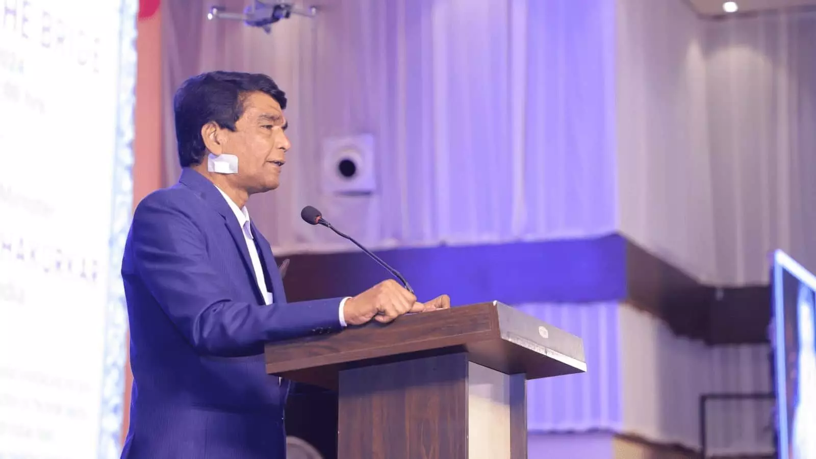 तस्वीर में नीले कोट में एक व्यक्ति पोडियम पर खड़े होकर बोलते हुए दिखाई दे रहे हैं। तस्वीर में नीले कोट में एक व्यक्ति पोडियम पर खड़े होकर बोलते हुए दिखाई दे रहे हैं।