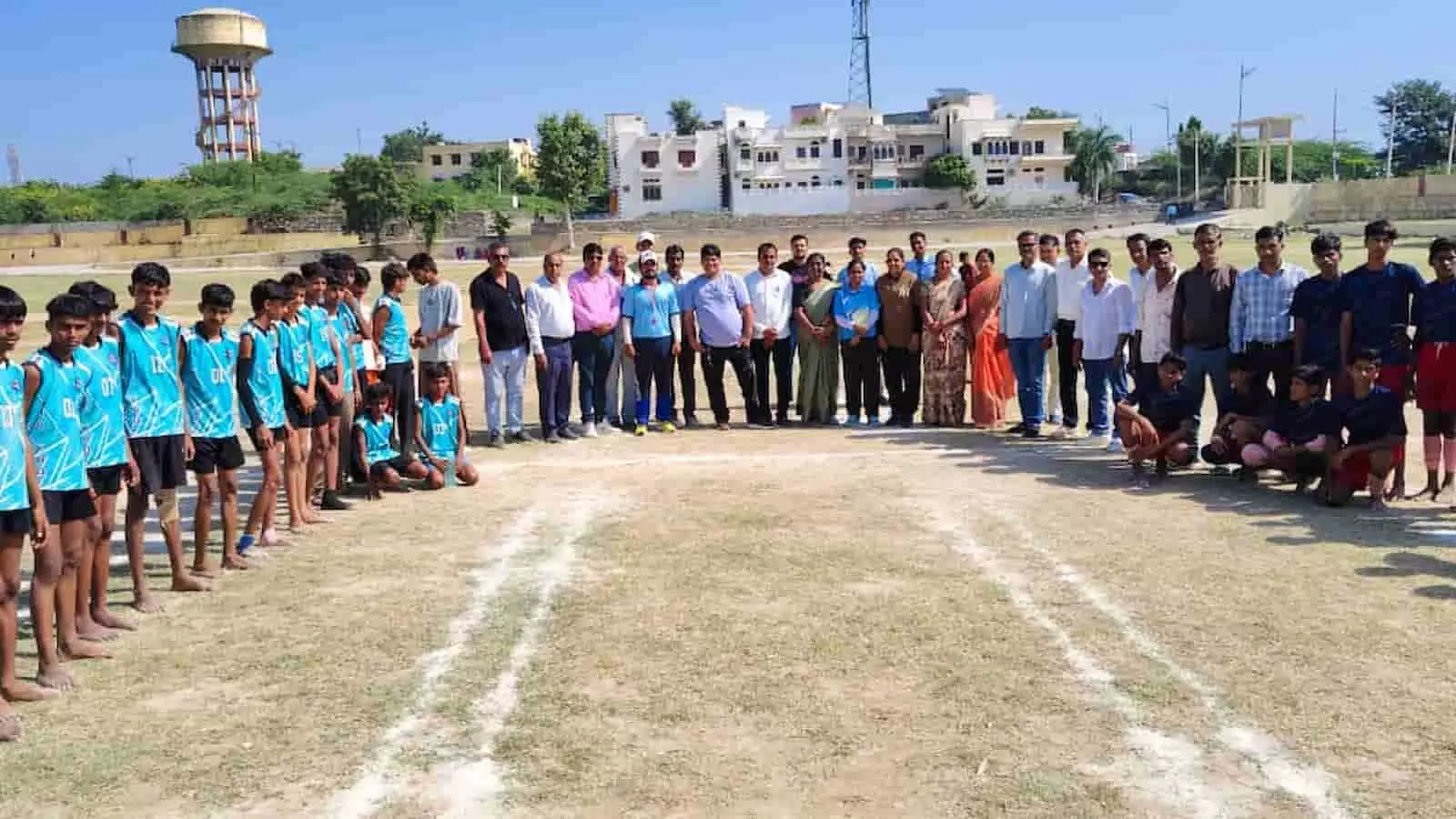 तस्वीर में खेल मैदान में आमने-सामने खड़ी खिलाड़ियों की टीमें और उनके पीछे खड़े अतिथियों का समूह दिखाई दे रहा है। तस्वीर में खेल मैदान में आमने-सामने खड़ी खिलाड़ियों की टीमें और उनके पीछे खड़े अतिथियों का समूह दिखाई दे रहा है।