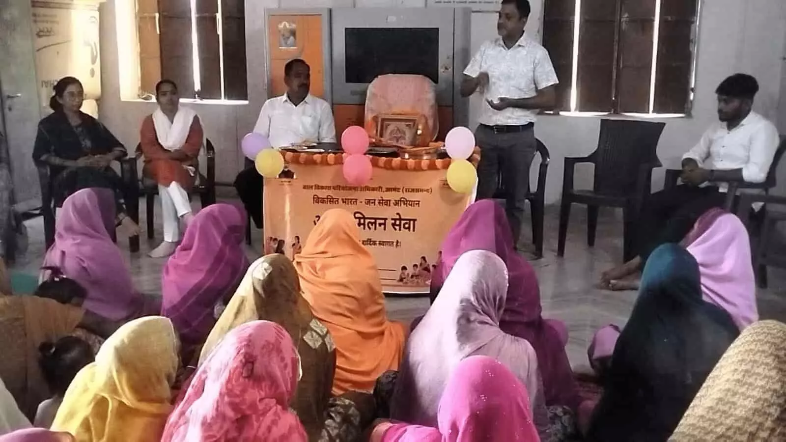 तस्वीर में कार्यक्रम के दौरान आगे बैठी महिलाओं और पीछे खड़े वक्ताओं तथा अधिकारियों का समूह दिखाई दे रहा है। तस्वीर में कार्यक्रम के दौरान आगे बैठी महिलाओं और पीछे खड़े वक्ताओं तथा अधिकारियों का समूह दिखाई दे रहा है।