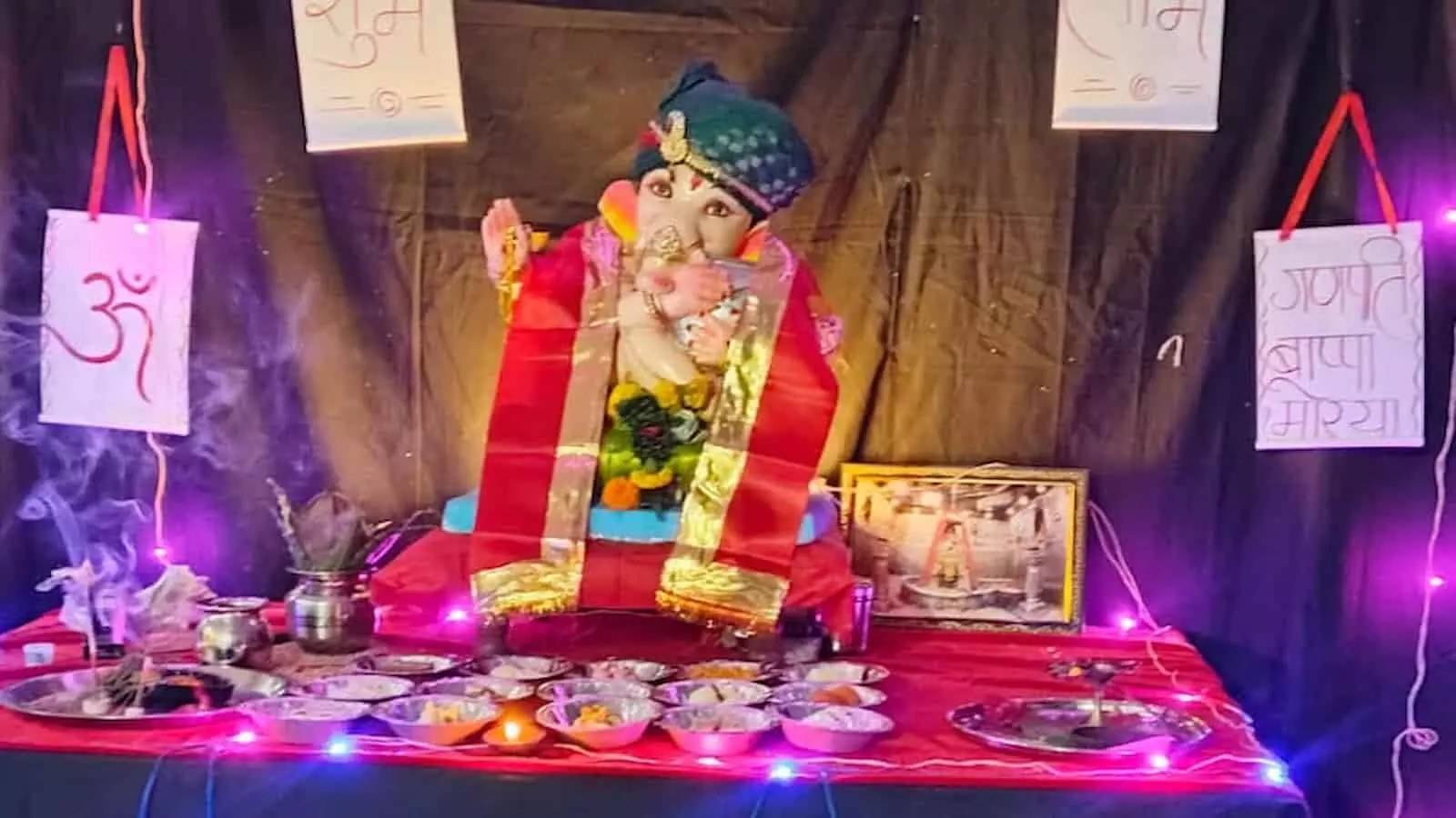तस्वीर में रंगीन लाइटों और सजावट के बीच भगवान गणेश की मूर्ति और पूजन सामग्री रखी दिखाई दे रही है। तस्वीर में रंगीन लाइटों और सजावट के बीच भगवान गणेश की मूर्ति और पूजन सामग्री रखी दिखाई दे रही है।