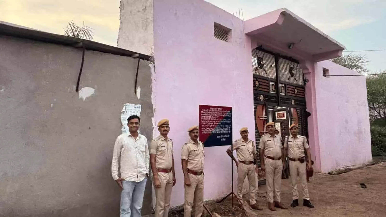 तस्वीर में गुलाबी रंग के मकान के मुख्य द्वार के सामने वर्दी में खड़े पुलिसकर्मियों का समूह दिखाई दे रहा है। तस्वीर में गुलाबी रंग के मकान के मुख्य द्वार के सामने वर्दी में खड़े पुलिसकर्मियों का समूह दिखाई दे रहा है।