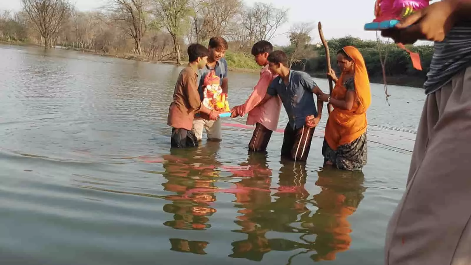 तस्वीर में कुछ लोग पानी के अंदर खड़े होकर गणेश जी की मूर्ति को विसर्जित करते दिखाई दे रहे हैं। तस्वीर में कुछ लोग पानी के अंदर खड़े होकर गणेश जी की मूर्ति को विसर्जित करते दिखाई दे रहे हैं।