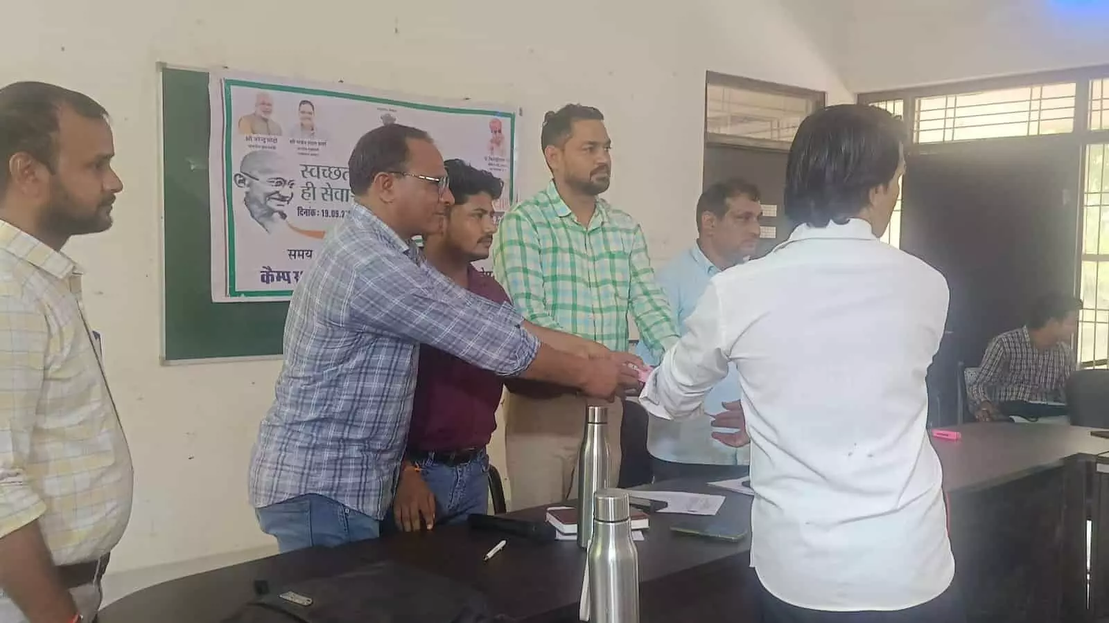 सवाई माधोपुर शिविर में अधिकारी टेबल के पास खड़े होकर व्यक्ति को दस्तावेज प्रदान कर रहे हैं। सवाई माधोपुर शिविर में अधिकारी टेबल के पास खड़े होकर व्यक्ति को दस्तावेज प्रदान कर रहे हैं।
