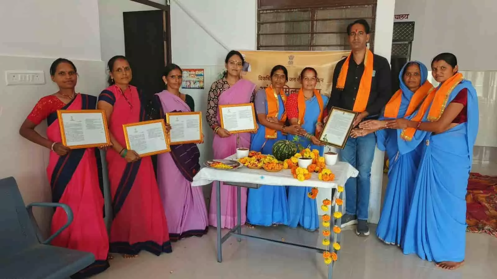 तस्वीर में बाएं से दाएं गुलाबी और नीले कपड़ों में महिलाएं तथा एक व्यक्ति हाथ में प्रमाण पत्र पकड़े हुए खड़े हैं। तस्वीर में बाएं से दाएं गुलाबी और नीले कपड़ों में महिलाएं तथा एक व्यक्ति हाथ में प्रमाण पत्र पकड़े हुए खड़े हैं।