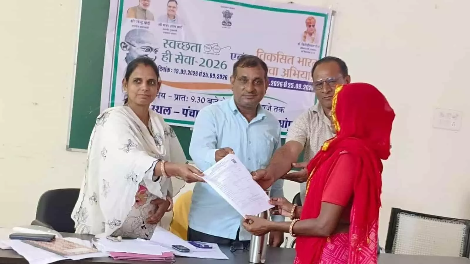 तस्वीर में अधिकारी और एक महिला ग्राम पंचायत भवन में पेंशन दस्तावेज पकड़ते हुए। तस्वीर में अधिकारी और एक महिला ग्राम पंचायत भवन में पेंशन दस्तावेज पकड़ते हुए।