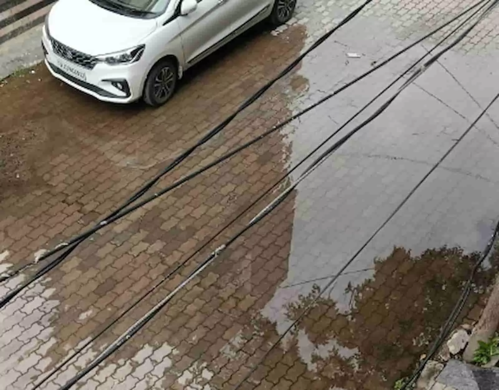 तस्वीर में सड़क पर फैला पानी और एक सफेद कार दिखाई दे रही है. तस्वीर में सड़क पर फैला पानी और एक सफेद कार दिखाई दे रही है.