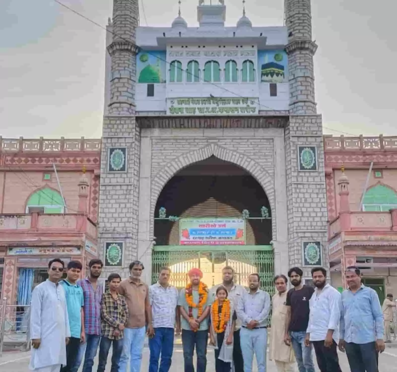 कपासन दरगाह के मुख्य द्वार के सामने खड़े होकर फूलों की माला पहने ट्रेनर उज्ज्वल दाधीच, अलवीरा बानो और अन्य लोग। कपासन दरगाह के मुख्य द्वार के सामने खड़े होकर फूलों की माला पहने ट्रेनर उज्ज्वल दाधीच, अलवीरा बानो और अन्य लोग।