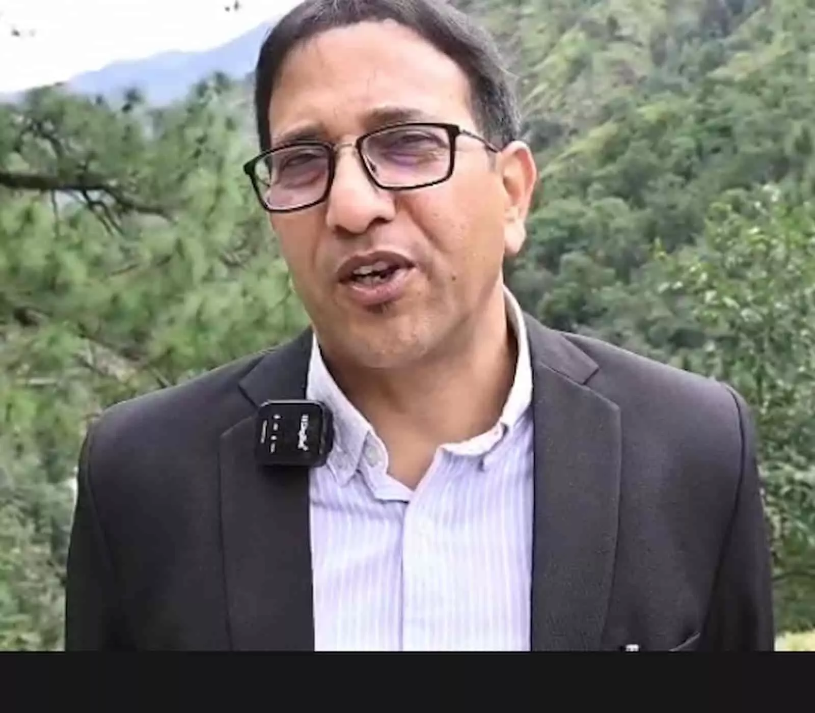 तस्वीर में चश्मा और काला कोट पहने व्यक्ति पहाड़ों की पृष्ठभूमि में बोलता दिख रहा है। तस्वीर में चश्मा और काला कोट पहने व्यक्ति पहाड़ों की पृष्ठभूमि में बोलता दिख रहा है।