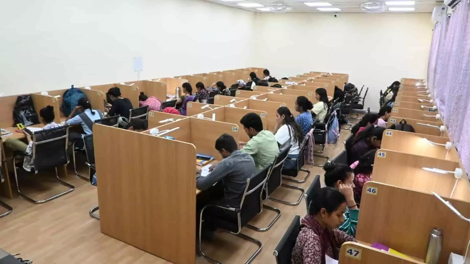 लाइब्रेरी के अध्ययन कक्ष में कतारबद्ध टेबल-कुर्सियों पर बैठकर पढ़ते हुए छात्र और छात्राएं। लाइब्रेरी के अध्ययन कक्ष में कतारबद्ध टेबल-कुर्सियों पर बैठकर पढ़ते हुए छात्र और छात्राएं।