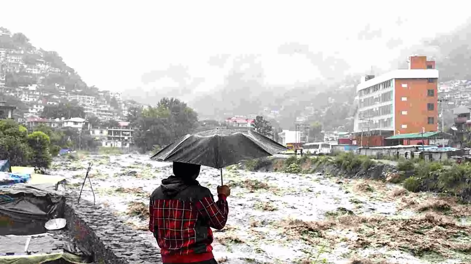 उफनती नदी के पास छाता लिए व्यक्ति उत्तर भारत में वर्षा के दौरान। उफनती नदी के पास छाता लिए व्यक्ति उत्तर भारत में वर्षा के दौरान।
