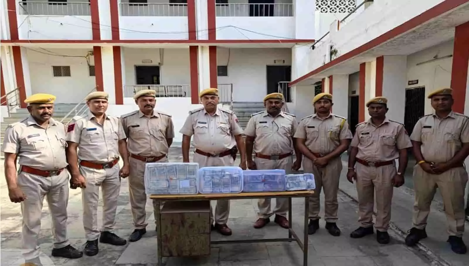 बाएं से दाएं खड़े आठ राजस्थान पुलिसकर्मी टेबल पर रखे नकदी और सामान के साथ दिखाई दे रहे हैं। बाएं से दाएं खड़े आठ राजस्थान पुलिसकर्मी टेबल पर रखे नकदी और सामान के साथ दिखाई दे रहे हैं।