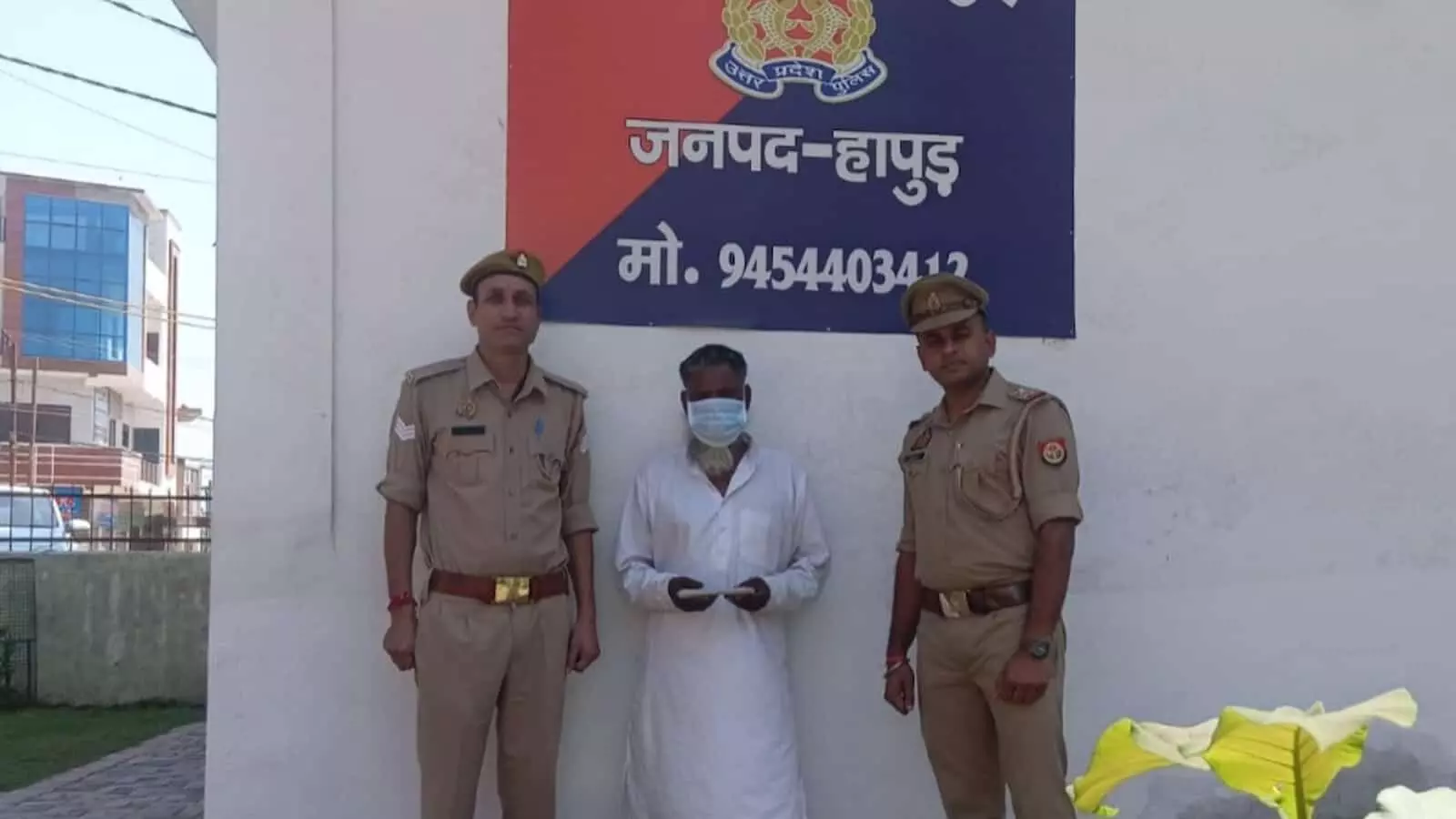 हापुड़ में पुलिस स्टेशन के बोर्ड के सामने दो पुलिस अधिकारियों की हिरासत में खड़ा व्यक्ति। हापुड़ में पुलिस स्टेशन के बोर्ड के सामने दो पुलिस अधिकारियों की हिरासत में खड़ा व्यक्ति।