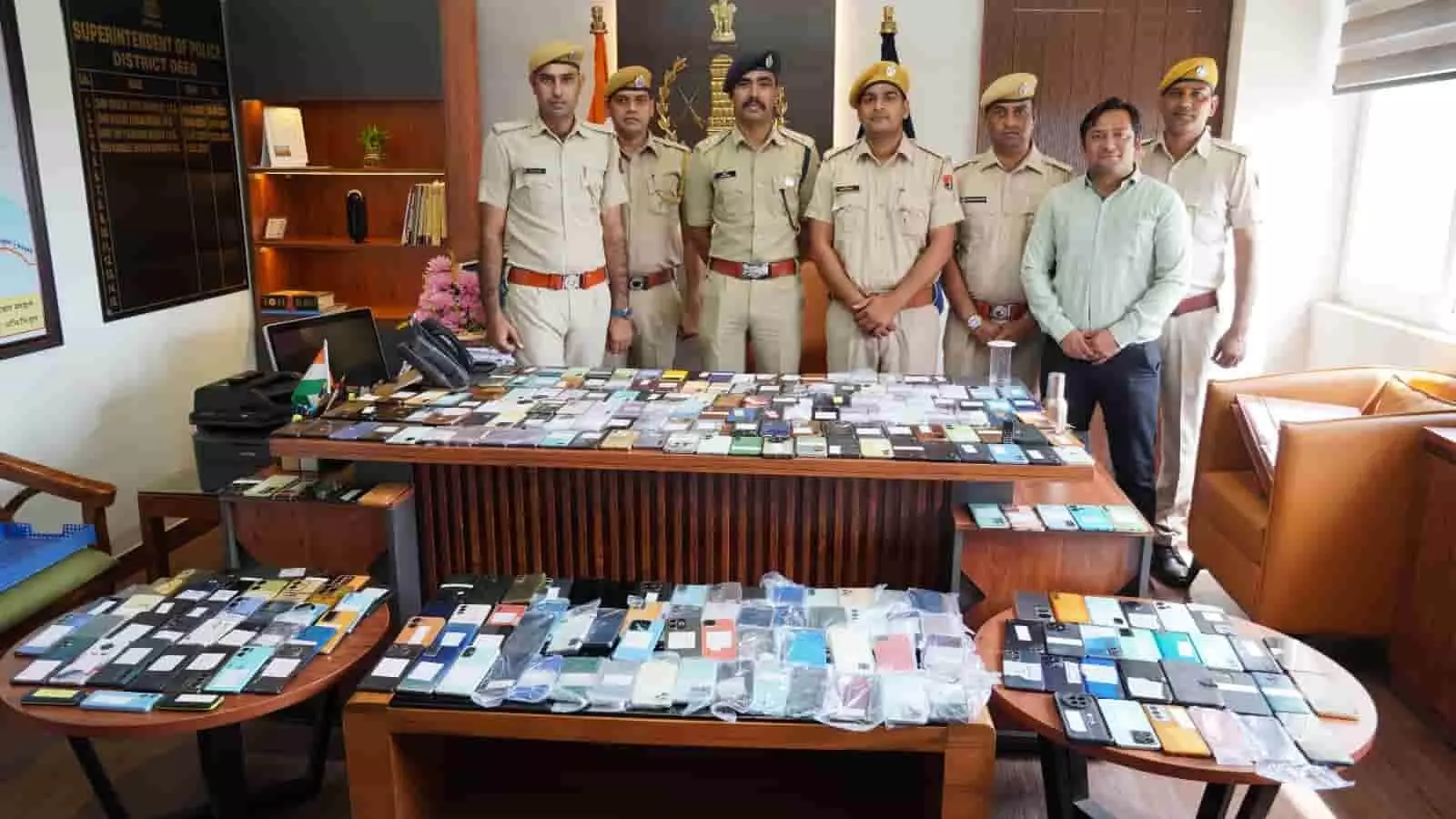 तस्वीर में पुलिसकर्मी और एक व्यक्ति मेज पर सजे बरामद मोबाइल फोन के पीछे खड़े दिखाई दे रहे हैं। तस्वीर में पुलिसकर्मी और एक व्यक्ति मेज पर सजे बरामद मोबाइल फोन के पीछे खड़े दिखाई दे रहे हैं।