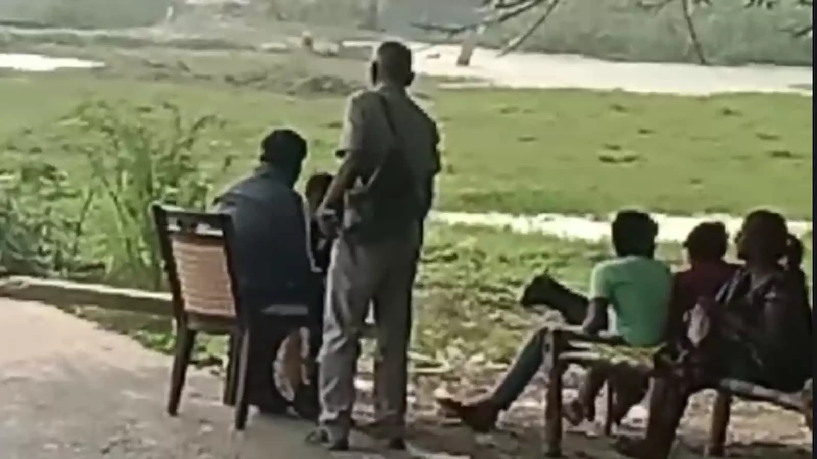 तस्वीर में एक व्यक्ति खड़ा है और अन्य लोग पास में रखी कुर्सियों पर बैठे हैं। तस्वीर में एक व्यक्ति खड़ा है और अन्य लोग पास में रखी कुर्सियों पर बैठे हैं।