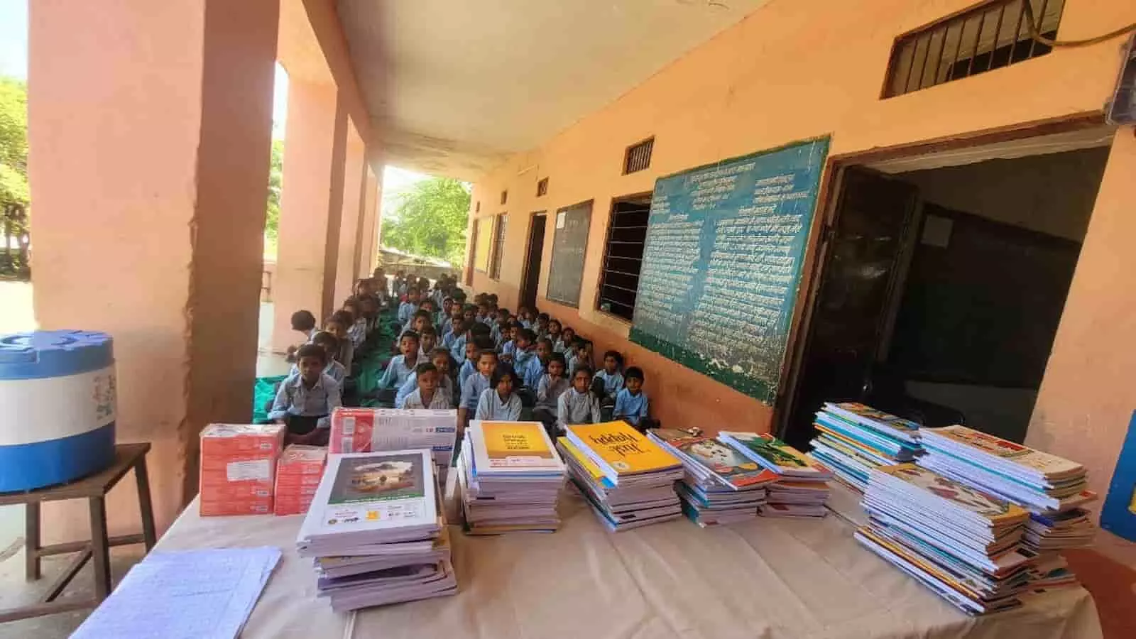 तस्वीर में झाड़ोल के स्कूल में मेज पर रखी शिक्षण सामग्री और नीचे बैठे छात्र दिख रहे हैं। तस्वीर में झाड़ोल के स्कूल में मेज पर रखी शिक्षण सामग्री और नीचे बैठे छात्र दिख रहे हैं।