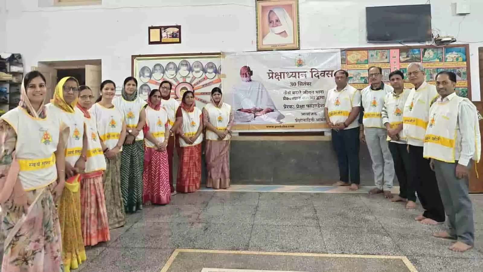 तस्वीर में बाएं से दाएं खड़े महिलाएं और पुरुष प्रेक्षा ध्यान कार्यशाला के बैनर के पास समूह में उपस्थित हैं।
