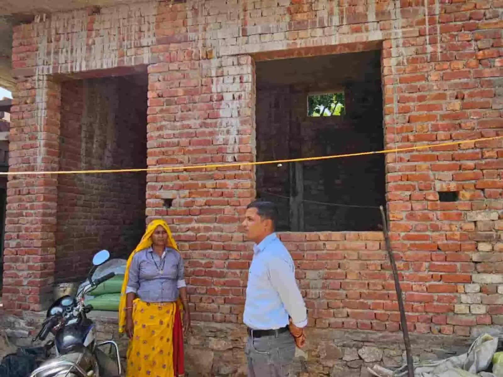 तस्वीर में बायीं ओर एक महिला पीली ओढ़नी में और दायीं ओर अधिकारी नीली कमीज में निर्माणाधीन भवन के सामने खड़े हैं। तस्वीर में बायीं ओर एक महिला पीली ओढ़नी में और दायीं ओर अधिकारी नीली कमीज में निर्माणाधीन भवन के सामने खड़े हैं।
