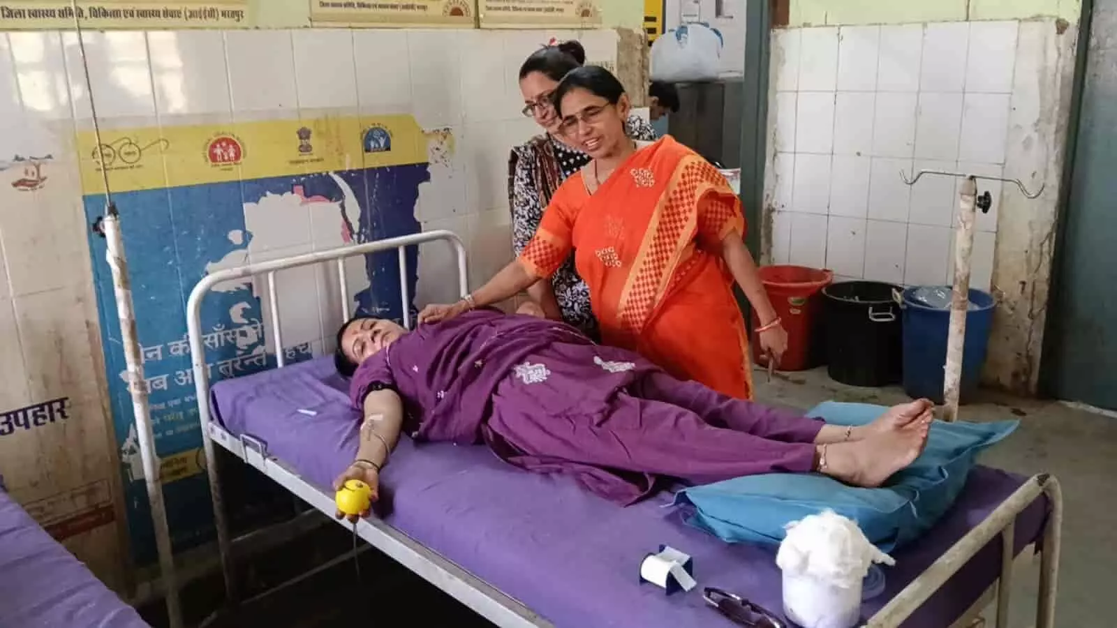 तस्वीर में दिख रही महिला बेड पर लेटी है और स्वास्थ्यकर्मी उसकी देखभाल कर रहे हैं। तस्वीर में दिख रही महिला बेड पर लेटी है और स्वास्थ्यकर्मी उसकी देखभाल कर रहे हैं।