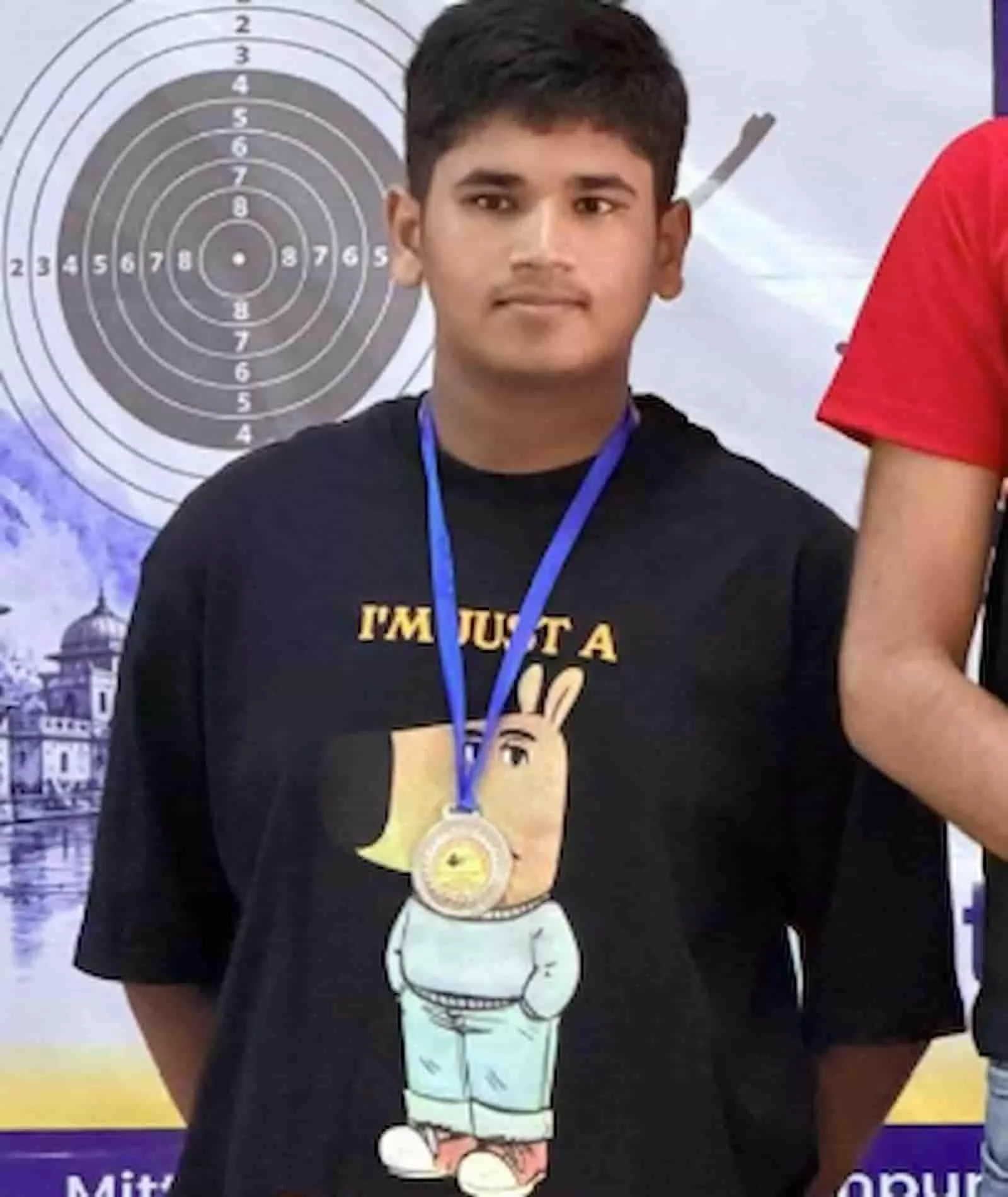 तस्वीर में गले में पदक पहने भव्य मोदी बैकग्राउंड में लगे शूटिंग टारगेट बोर्ड के आगे खड़े हैं। तस्वीर में गले में पदक पहने भव्य मोदी बैकग्राउंड में लगे शूटिंग टारगेट बोर्ड के आगे खड़े हैं।