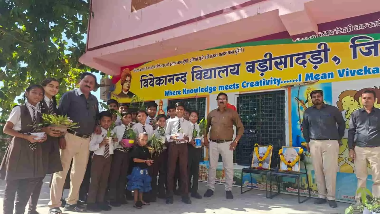 तस्वीर में विद्यालय भवन के बाहर शिक्षक और विद्यार्थी गमलों में छोटे पौधे लिए खड़े हैं। तस्वीर में विद्यालय भवन के बाहर शिक्षक और विद्यार्थी गमलों में छोटे पौधे लिए खड़े हैं।