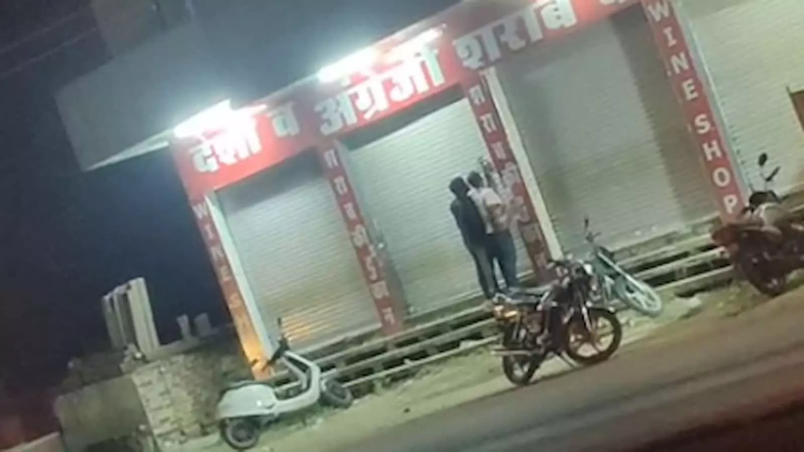 तस्वीर में दिख रही शराब दुकान का शटर बंद है और बाहर दो लोग तथा दोपहिया वाहन खड़े हैं। तस्वीर में दिख रही शराब दुकान का शटर बंद है और बाहर दो लोग तथा दोपहिया वाहन खड़े हैं।