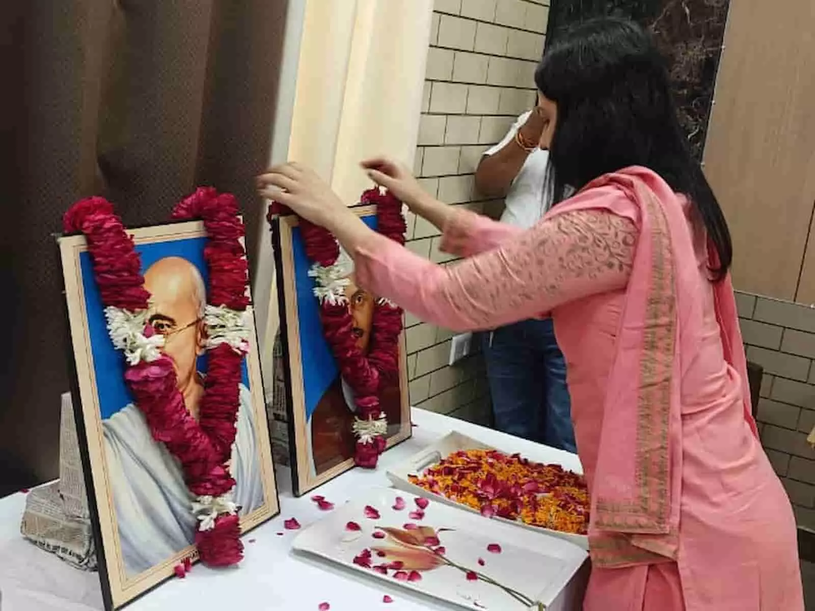 तस्वीर में बायीं ओर रखे चित्रों पर दायीं ओर खड़ी महिला अधिकारी पुष्पमाला पहनाती दिख रही हैं। तस्वीर में बायीं ओर रखे चित्रों पर दायीं ओर खड़ी महिला अधिकारी पुष्पमाला पहनाती दिख रही हैं।