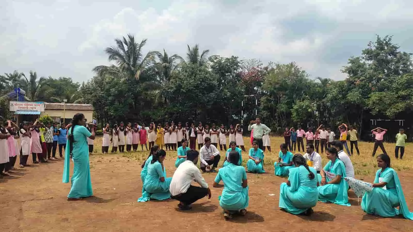 तस्वीर में नीली पोशाक पहने छात्र प्रशिक्षक मैदान में बैठकर नुक्कड़ नाटक करते दिख रहे हैं। तस्वीर में नीली पोशाक पहने छात्र प्रशिक्षक मैदान में बैठकर नुक्कड़ नाटक करते दिख रहे हैं।