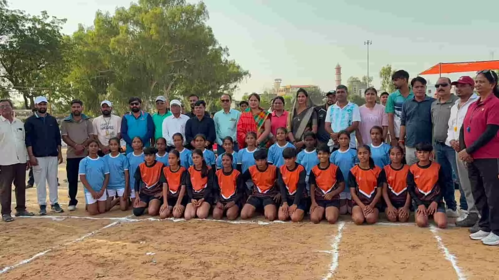तस्वीर में बालिका कबड्डी खिलाड़ी और अतिथि मैदान में एक समूह में खड़े और बैठे हुए हैं। तस्वीर में बालिका कबड्डी खिलाड़ी और अतिथि मैदान में एक समूह में खड़े और बैठे हुए हैं।